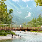Kappa Bridge 河童橋 – The Scenic Heart of Kamikochi People swim in the river beneath Kappa Bridge, enjoying the scenic view and refreshing waters.