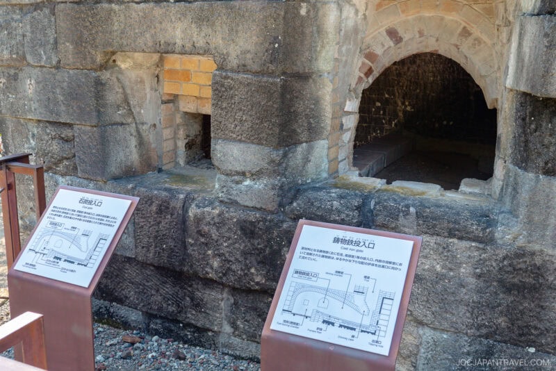 A historic brick and stone kiln, the Nirayama Reverberatory Furnace features two information boards in front with diagrams and Japanese text explaining the kiln’s arched openings, weathered stonework, and unique structure.