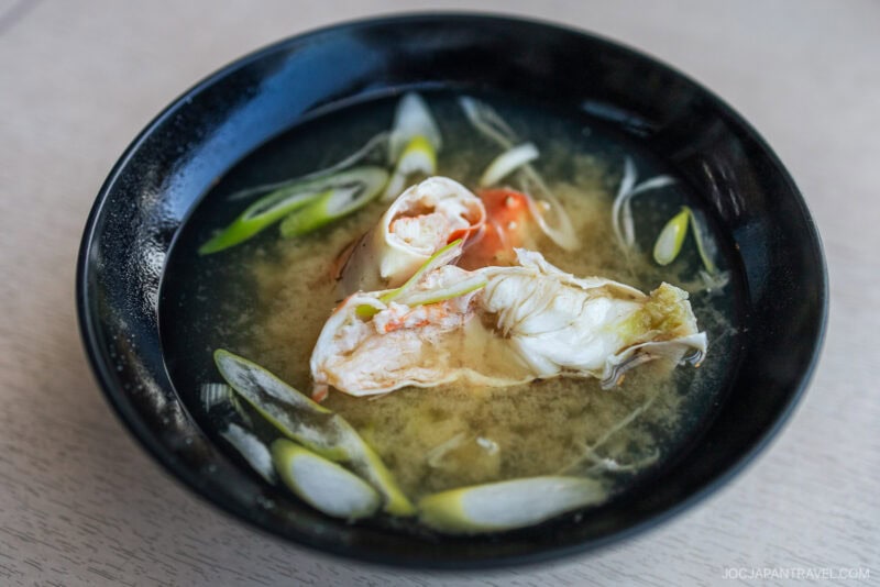 A black bowl filled with miso soup, topped with a piece of crab and garnished with sliced green onions, this dish is a highlight in any Hokkaido food guide, set beautifully on a light-colored surface.