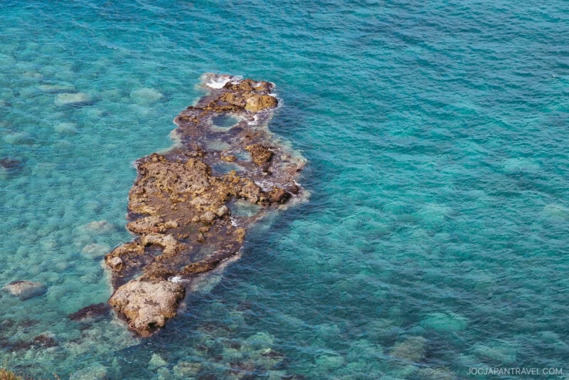 A rocky formation surrounded by clear turquoise water in the sea near Yoichi, with coral and rocks visible beneath the surface.