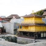 Legoland Nagoya Travel Guide A detailed miniature model of a traditional Japanese temple with yellow-golden walls and a tiered roof, inspired by Nagoya architecture, is surrounded by stone walls and set near a pond—perfect for any Legoland Nagoya travel guide.
