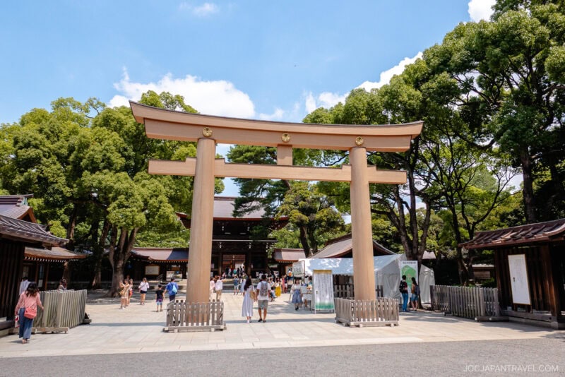 Large wooden torii gate at the entrance of Meiji Jingu Shrine, surrounded by trees and visitors walking around on a sunny day.