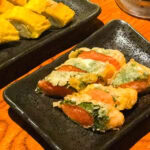 Negibouzu Izakaya (ねぎぼうず) – A Taste of Kumamoto’s Local Flavors Close-up of tempura vegetables and fish served on black rectangular plates at Negibouzu Izakaya, with one plate containing yellow pieces and another featuring green and orange tempura items on a wooden table.
