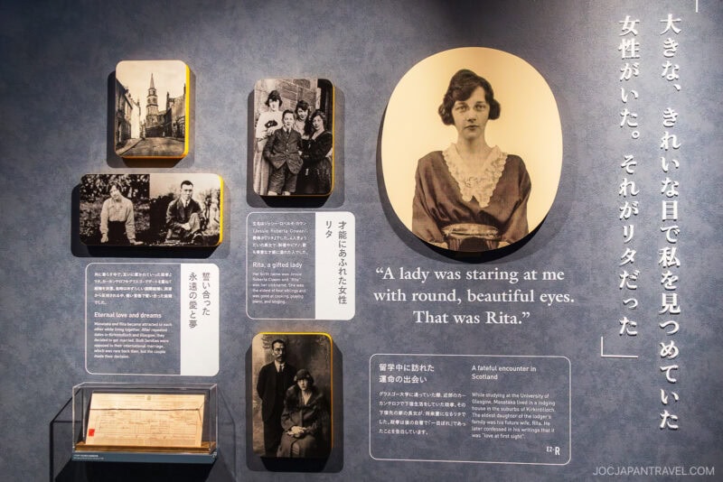 A museum exhibit at the Nikka Whisky Yoichi Distillery features vintage photos, a portrait of a young woman, and quotes about Rita on a gray wall, with Japanese text and the English quote: “A lady was staring at me with round, beautiful eyes. That was Rita.”.