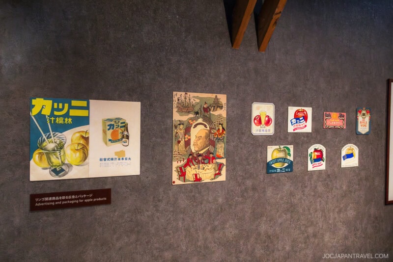 A wall display of vintage Japanese advertisements and packaging for apple products, including colorful posters, labels, and illustrations—some alongside memorabilia from the Nikka Whisky Yoichi Distillery—arranged in a horizontal row.
