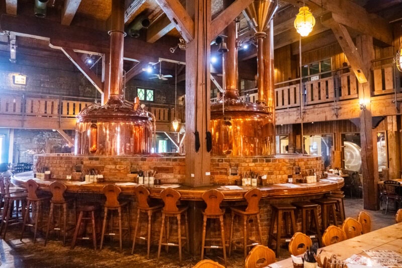 A rustic otaru brewery interior with large copper brewing tanks, a brick bar, wooden stools, and exposed wooden beams, creating a warm, inviting atmosphere.