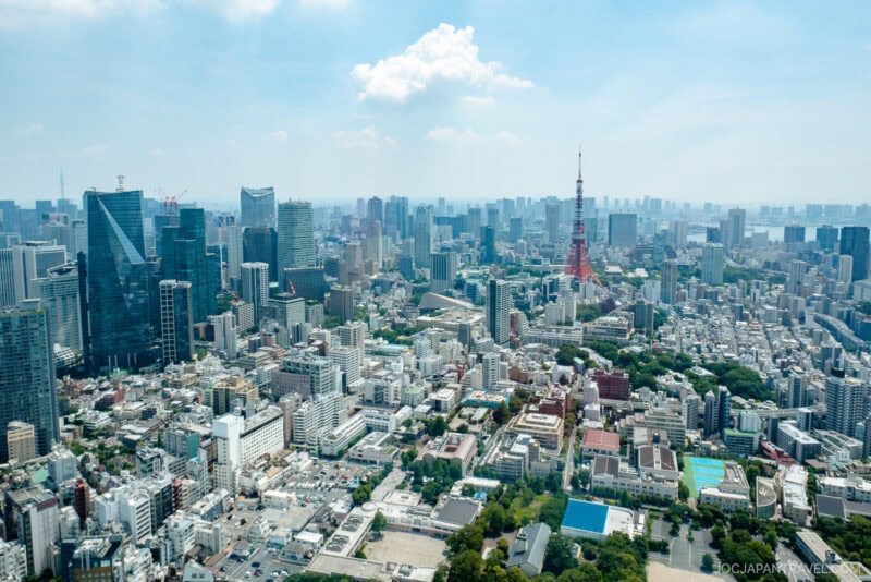 Aerial view of Tokyo&rsquo;s cityscape with dense high-rise buildings, the iconic Tokyo Tower in the distance, and a hazy sky overhead captures a stunning tokyo city view.