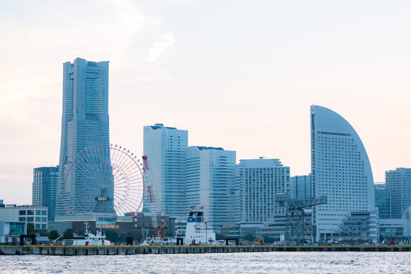 Skyline of Yokohama, Japan, featuring modern skyscrapers, a large ferris wheel, a ship docked by the waterfront, and the distinctively curved InterContinental Yokohama Grand hotel.