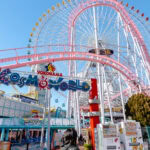 Yokohama Cosmo World (よこはまコスモワールド) – A Waterfront Amusement Park Entrance to Yokohama Cosmo World amusement park with colorful signage welcomes visitors, while the iconic pink Ferris wheel and a thrilling roller coaster stand tall in the background under a clear blue sky.