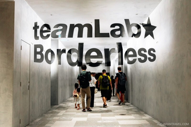 People walk through a minimalist white hallway at teamLab Borderless, where bold black text on the walls and ceiling immerses visitors in the museum’s distinctive aesthetic.