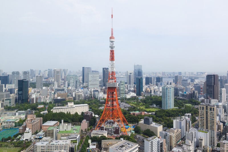 Tokyo cityscape featuring Tokyo Tower, an orange and white observation tower, with modern buildings and greenery under a cloudy sky&mdash;just a short trip from the immersive digital art of teamLab Borderless.