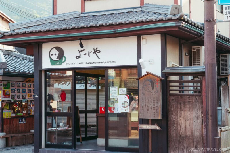 The Yojiya Cafe exterior in Sagano Arashiyama, Kyoto, Japan, showcases a traditional-style building paired with a modern glass storefront and the signature Yojiya Cafe sign featuring its stylized face logo.