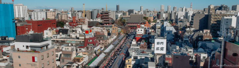 A panoramic cityscape of Tokyo featuring a bustling street lined with shops and crowds, surrounded by modern buildings, with the historic Senso-ji Temple visible in the center background.