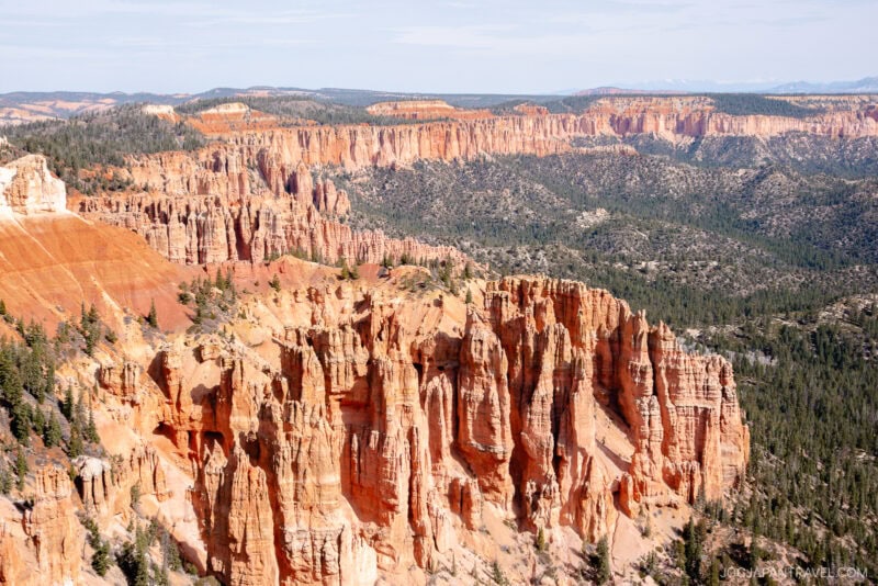 Wide view of Bryce Canyon National Park, featuring its iconic orange and red rock formations, hoodoos, and green pine trees under a partly cloudy sky.