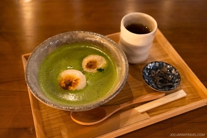 A bowl of matcha green tea with toasted marshmallows, served on a wooden tray alongside tea, pickles, a spoon, and chopsticks&mdash;a must-try Kyoto what to eat experience.