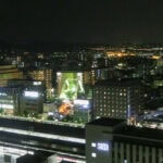 Kyoto Station (京都駅) – A Modern Gateway to the Ancient Capital A nighttime cityscape featuring illuminated buildings, bustling streets, and the well-lit Kyoto Station in the foreground, with distant city lights stretching across the horizon.