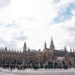 Top Things to Do in London for Families over 6 Days Crowds of people walk in front of the Palace of Westminster and Big Ben in London on a cloudy day, with the iconic clock tower visible on the left and London’s stunning gothic architecture dominating the scene.
