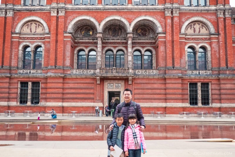 A man and two children posing for a picture in front of a large brick building in London.