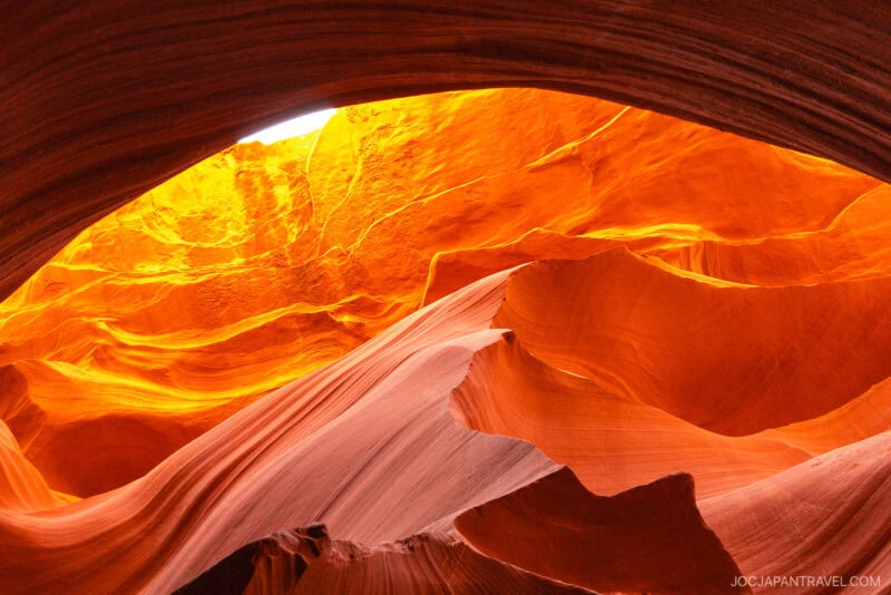 Sunlight illuminates the smooth, flowing red and orange sandstone walls of Lower Antelope Canyon, highlighting intricate textures and natural patterns inside the narrow slot canyon.