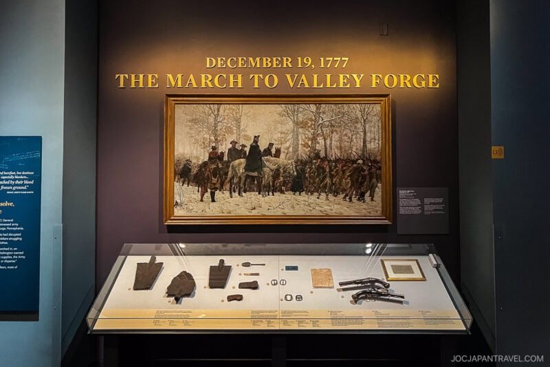 Exhibit display with a painting labeled The March to Valley Forge, December 19, 1777, depicting soldiers in winter near Philadelphia, with historical artifacts in a glass case below.