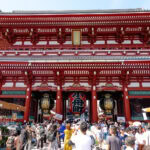 Sensoji Temple (浅草寺): Tokyo’s Most Iconic Buddhist Landmark Large crowd gathers in front of the vibrant red and white Thunder Gate (Kaminarimon) at Senso-ji Temple in Tokyo, Japan, with large lanterns hanging beneath the ornate roof on a sunny day.
