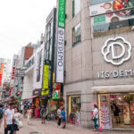 Center Gai (センター街) – Shibuya’s Hub of Food, Fashion, and Nightlife A busy street in Japan’s Shibuya Center Gai with people walking, colorful shop signs, and a large “IT’S DEMO” store on the corner. The lively atmosphere is filled with various shops and vibrant advertisements.