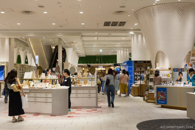 A modern department store interior at Shibuya Hikarie, with shoppers browsing cosmetics and skincare counters. Displays are neatly arranged, and large white columns support the high ceiling, creating a bright and spacious atmosphere.