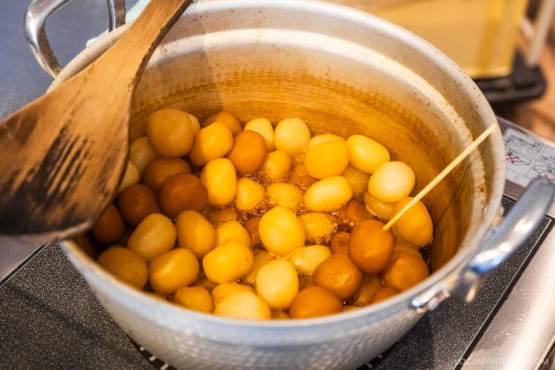 A pot of simmering dango (Japanese rice dumplings) in a savory yamagata-style brown sauce, with a wooden spatula resting on the side and a bamboo skewer inserted into some dumplings.