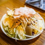 What to Eat in Yamagata Japan: From Yonezawa Beef to Cold Ramen A bowl filled with raw vegetables including cabbage, bean sprouts, and mushrooms, topped with a piece of raw meat, sits on a wooden table in a brightly lit yamagata dining setting.