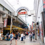 Ameyoko Market (アメ横) – Tokyo’s Bustling Street Market in Ueno A busy pedestrian street in Ameyoko Market, Tokyo, with people walking past shops, restaurants, and colorful Japanese signs. The Ameyokocho entrance arch rises above the lively street scene.