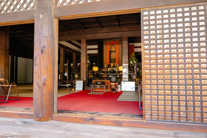 A view into the traditional interior of Nara Gango-ji temple, featuring tatami mats, a red carpet, ornate decorations, and an altar with golden objects, all framed by wooden beams and sliding lattice doors.