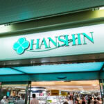 Hankyu and Hanshin – Umeda’s Iconic Osaka Department Stores A store entrance with a sign reading HANSHIN in teal letters and a clover logo above, welcoming shoppers into the brightly lit interior—a vibrant scene at the Hankyu and Hanshin Department Stores Osaka.