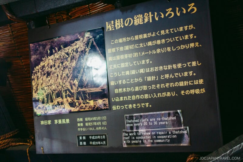 A sign with Japanese and English text and a photo of people building a large, traditional thatched roof at Kanda House Shirakawa-go. The English text explains that such roofs are created with help from the entire local community.