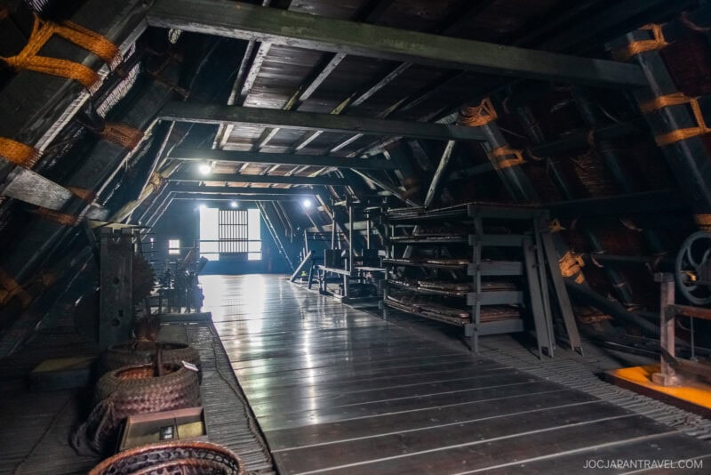 Dimly lit attic of Kanda House Shirakawa-go, a traditional Japanese home with wooden beams, woven baskets, and shelves, featuring sunlight streaming through a window at the far end.
