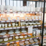 Shelves filled with neatly arranged white ceramic dishes, bowls, cups, and plates of various shapes and sizes in a well-lit Kappabashi Baise store.