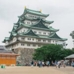 Nagoya Castle (名古屋城) – A Majestic Symbol of Tokugawa Legacy Nagoya Castle in Japan, with its iconic green-tiled roofs and golden ornaments, stands majestically as visitors stroll through the courtyard on a cloudy day.