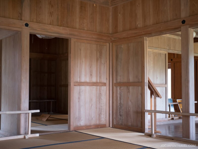Interior of a traditional Japanese room with wooden walls, sliding doors, and tatami mats, inspired by the elegance of Shikinaen. Minimal furnishings and natural light streaming through a window on the right create a serene ambiance.