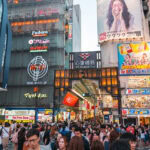 Shinsaibashi Shopping Street (心斎橋筋商店街) – Osaka’s Timeless Shopping Arcade A bustling street scene in Osaka Shinsaibashi, Japan, filled with crowds of people and surrounded by colorful storefronts, bright neon signs, and billboards in Japanese.