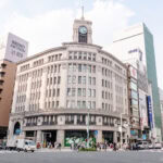 Shopping in Ginza (銀座) – Tokyo’s Premier Destination for Luxury, Craft, and Style A large, historic building with a clock tower stands at a busy city intersection in Ginza, surrounded by modern tall buildings and people shopping in Ginza, walking across wide crosswalks in daylight.