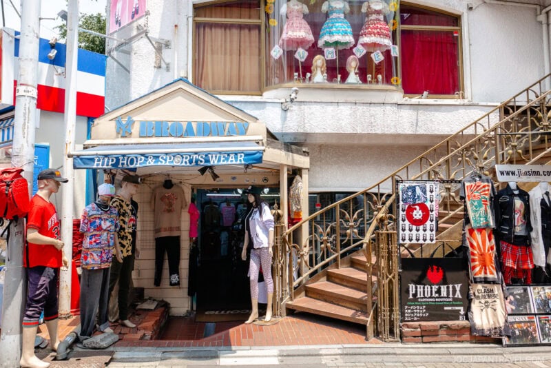 A clothing store on Takeshita Street Harajuku with a Broadway Hip Hop & Sports Wear sign, mannequins in colorful outfits outside, a staircase to the right, and fancy dresses displayed in an upstairs window.