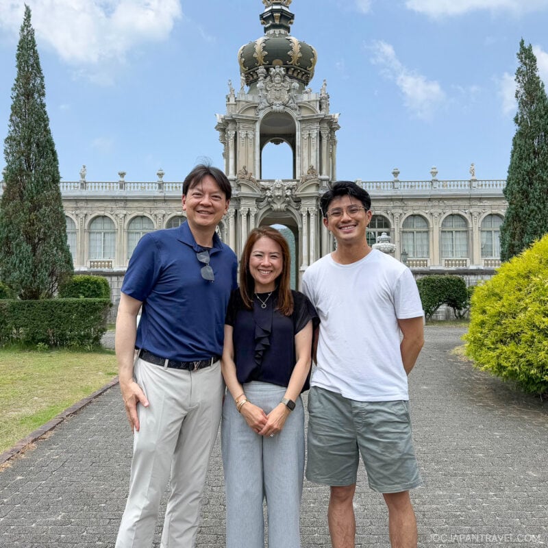 Three people stand smiling in front of the ornate Crown Gate at Dresden&rsquo;s Zwinger Palace, sharing their love for culture on a sunny day, with lush greenery and a clear blue sky in the background.