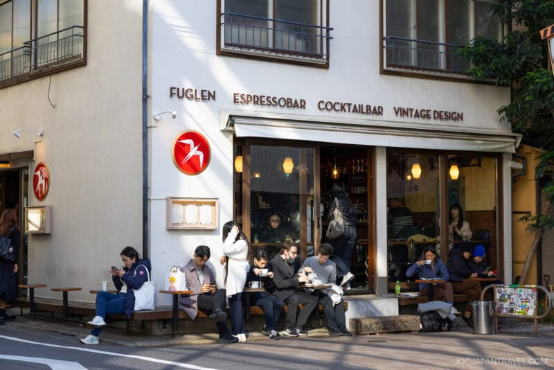 People sit outside Fuglen café on a sunny day, chatting, eating, or scrolling through their phones. With its large windows and vintage design, Fuglen stands out among the best cafes Tokyo offers in any Tokyo cafe guide.
