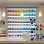 Must-Visit Stationery Stores In Tokyo A brightly lit store display features shelves of colorful ink bottles arranged in a rainbow gradient behind a white counter, with Japanese pens and sample inks on the counter—reminiscent of the finest stationery stores Tokyo has to offer.
