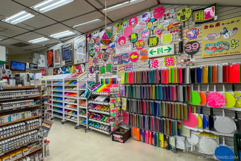 A colorful stationery store in Tokyo with neatly organized shelves of paper, notebooks, folders, and craft supplies. The walls are covered with bright, eye-catching signs in Japanese, featuring quality Japanese pens and beautiful Japanese paper.