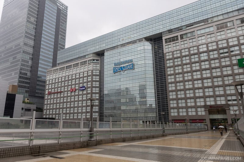 A modern cityscape with tall glass buildings, including one labeled Takashimaya Times Square, seen on a cloudy day—a popular spot for Tokyo activities and things to do Tokyo, even when it's a rainy day.