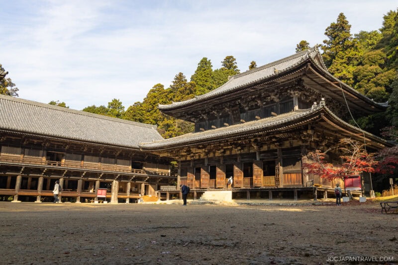 Large traditional wooden Japanese temple buildings with intricate roofs, surrounded by trees; a few people are walking and standing near Engyoji Temple&rsquo;s historic structures on a sunny day.