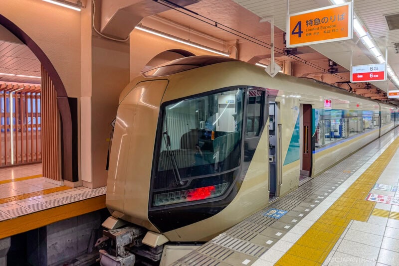 A sleek, modern Japanese limited express train with a gold and black exterior is stopped at an indoor station platform under orange lighting. Above, a sign displays platform number 4 for limited express trains—perfect for those with Japan train tickets.