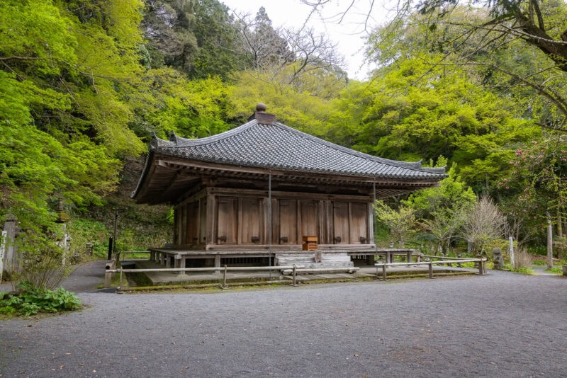 A traditional wooden Japanese temple with a tiled roof stands surrounded by lush green trees on the tranquil Kunisaki Peninsula, Oita—set along a gravel path in this sacred region’s serene, natural environment.