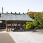 Miyazaki Shrine: Miyazaki's Oldest Shrine A traditional Japanese shrine, Miyazaki Shrine, features a large wooden gate, sloped green roof, and decorative beams, surrounded by trees and a gravel courtyard under a clear sky in Miyazaki.