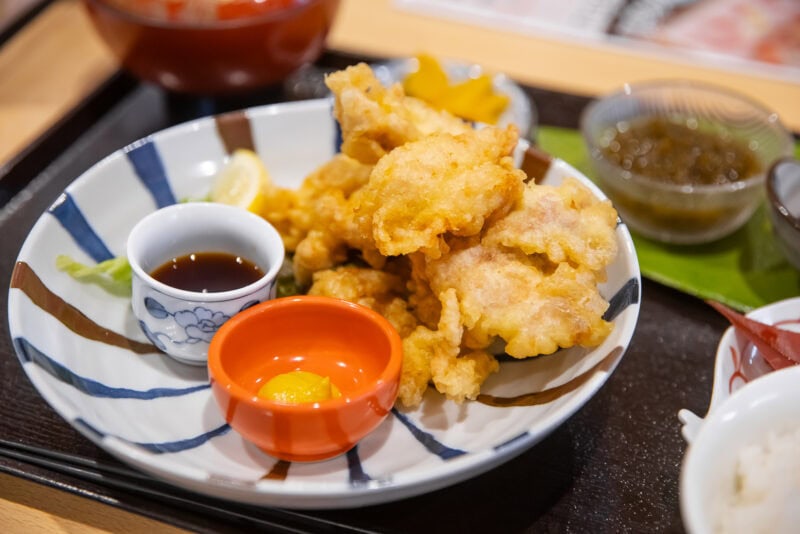 A plate of assorted tempura with dipping sauce, a lemon wedge, and a small portion of mustard—one of Oita’s must-try dishes—served alongside side dishes on a tray. A perfect choice for anyone wondering what to eat in Oita.